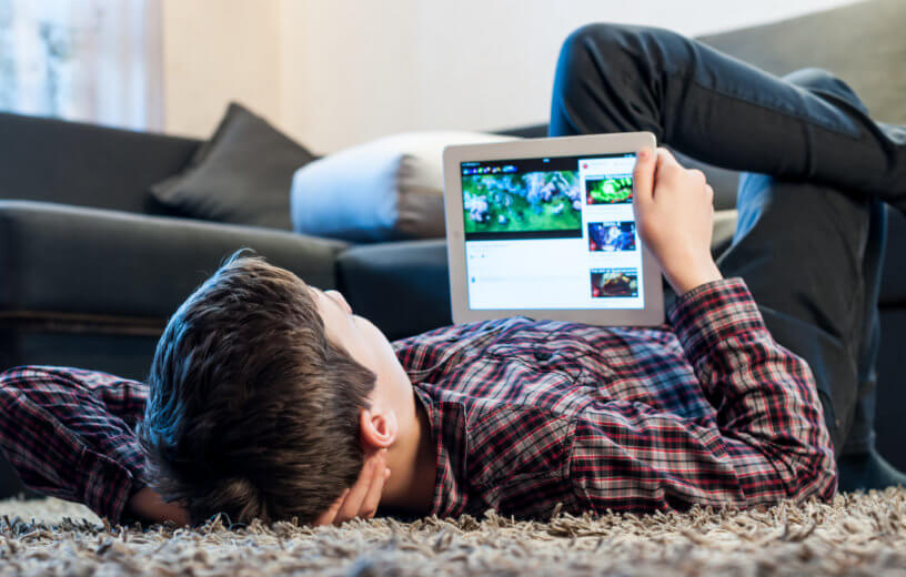 Teenager laying on the floor in the room looking at iPad or tablet