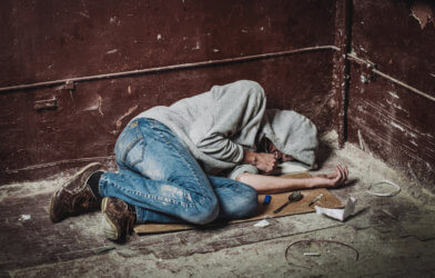 Drug addict with a syringe using drugs sitting on the floor
