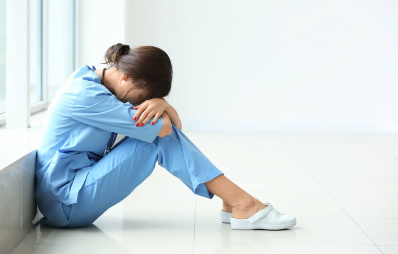 Tired female nurse sitting on floor in hospital