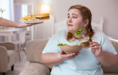 Tasty appealing hamburger enticing obese woman eating salad