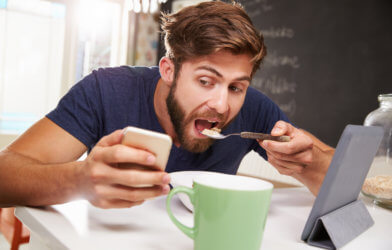 Man eating breakfast while looking at phone, tablet
