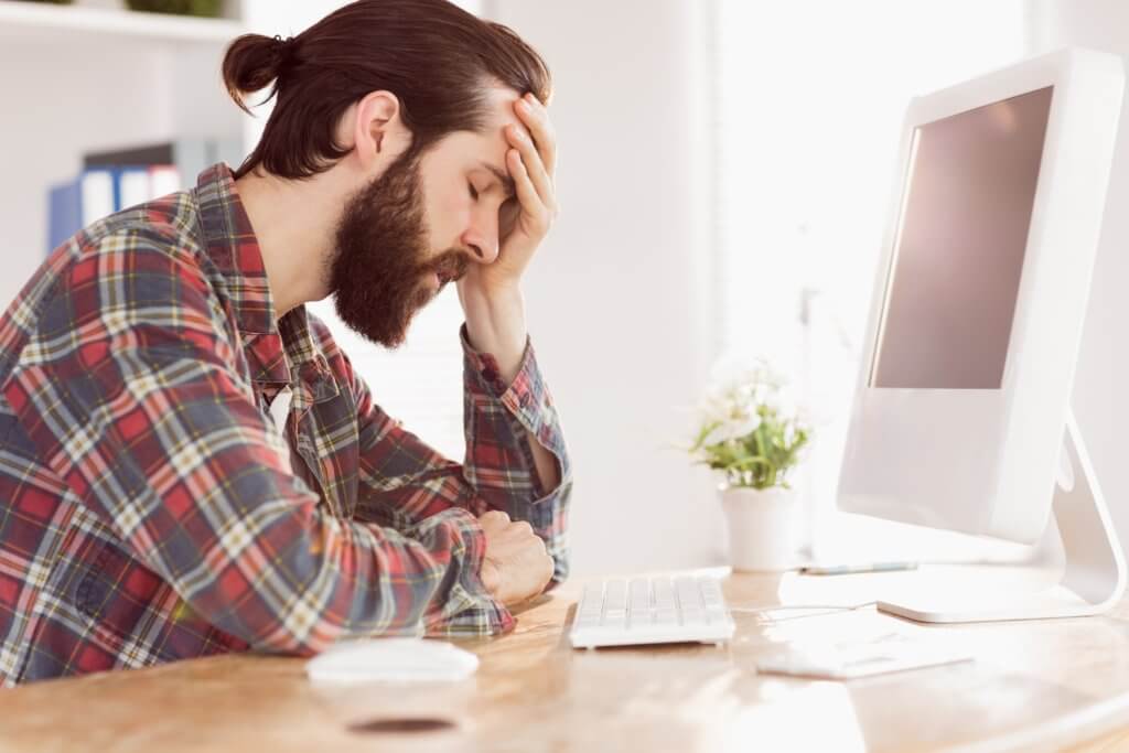 Stressed, upset millennial sitting at work computer
