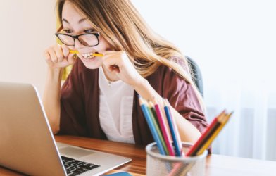 College student stress: Woman biting pencil while doing work on computer