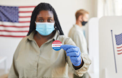 Woman in face mask holding "I Voted" sticker after voting on Election Day 2020
