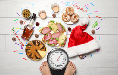 Holiday weight gain: Christmas food, sweets surrounding person weighing themselves on a scale