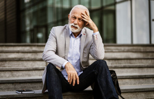 Older man tired, upset, exhausted on stairs outside office