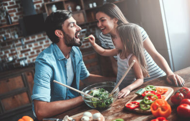 Little girl feeding her parents salad and vegetables